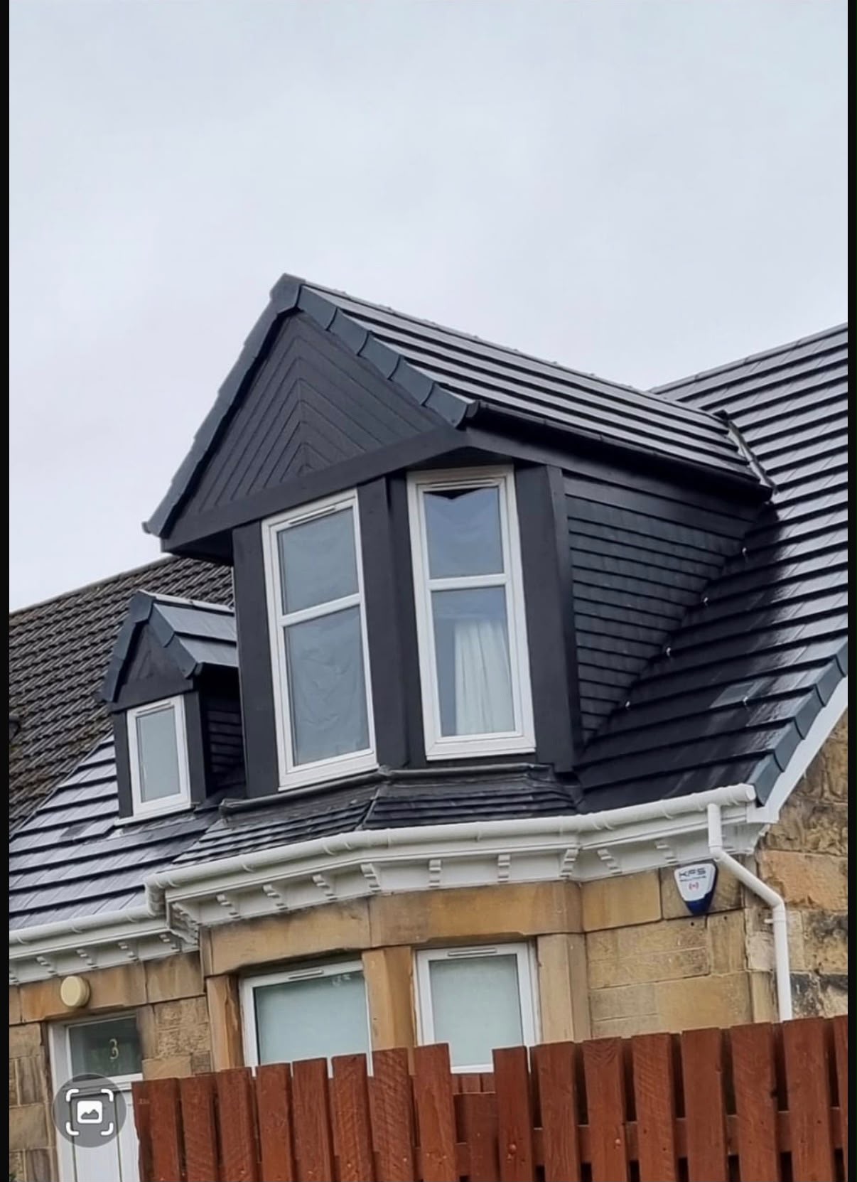 Close view of dark tiled dormers with white windows on a stone house