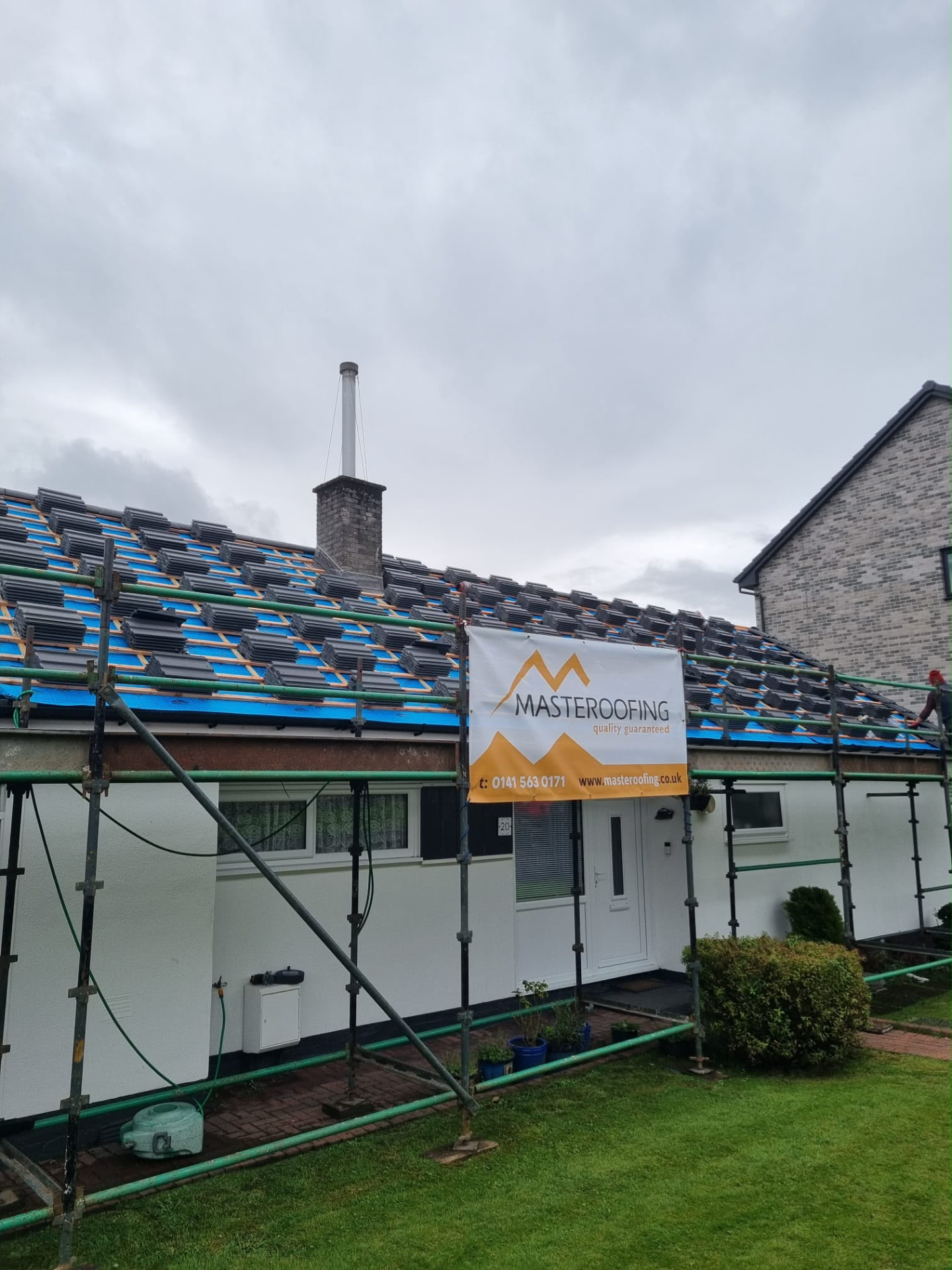 New grey roof tiles stacked on battens ready for fixing, Masteroofing banner on scaffolding