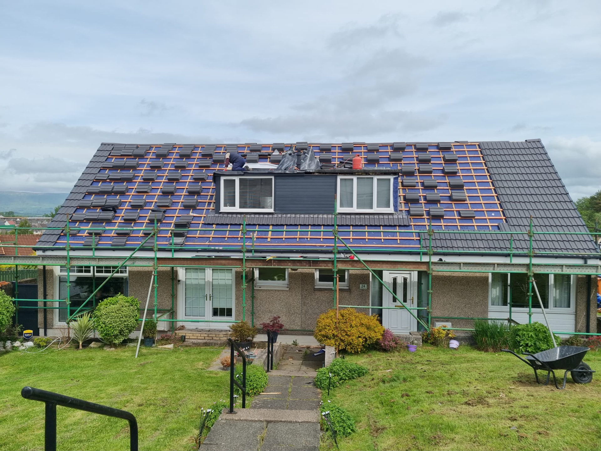 Roofer laying new grey tiles over battens and membrane on a semi-detached home