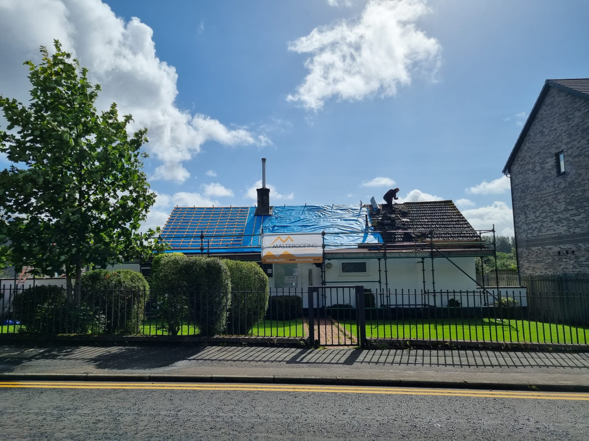 Bungalow roof stripped to battens and membrane with a Masteroofing banner on the scaffolding